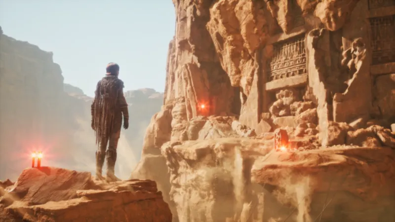 dune: awakening gameserver mieten – dein preisvergleich | 1 Eine Person im Anzug steht auf einem Felsvorsprung in einer sonnenbeschienenen Schlucht und blickt auf uralte, in Stein gehauene Strukturen. Rot glühende Lichter säumen die Felsen und werfen ein rätselhaftes Licht, das an Dune erinnert: Awakening Server's mysteriöser Atmosphäre.